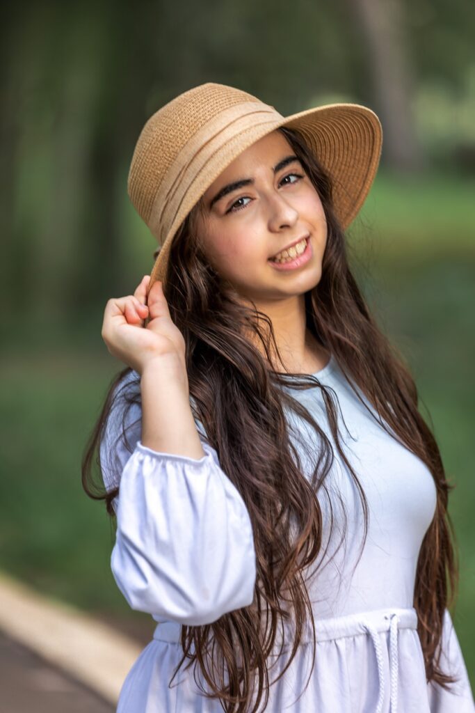 צילומי בת מצווה מתבגרת עם בפארק עם שמלה לבנה וכובע