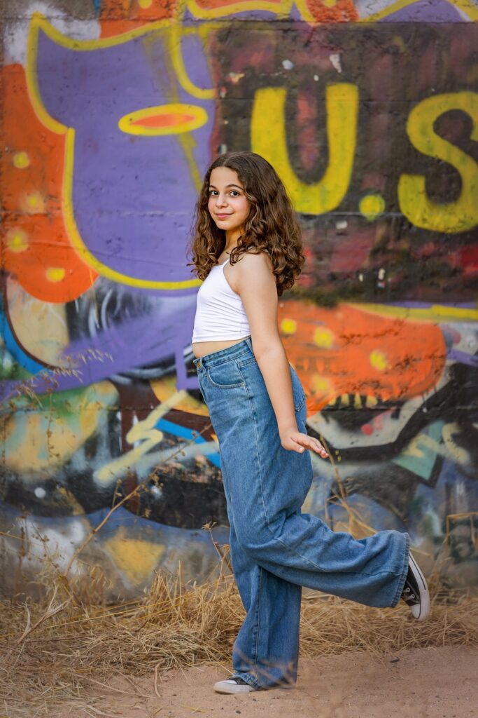 צילומי בת מצווה מתבגרת עומדת מרימה רגל מאחריה יש קיר מצויר