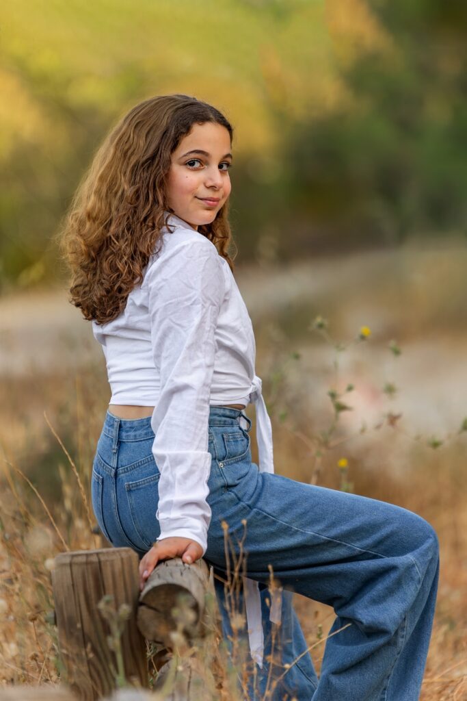 צילומי בת מצווה של מתבגרת בפארק עם גינס יושבת על גזע