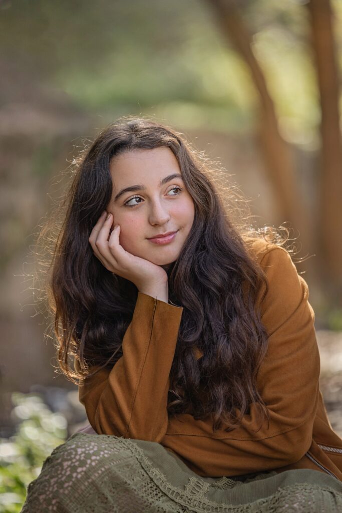 צילומי בת מצווה מתבגרת עם בפארק יושבת עם יד בפנים