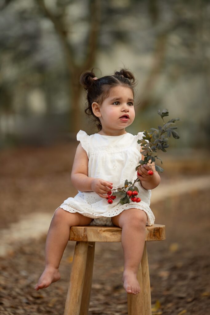 בת שנתיים יושבת על שרפרף בטבע עם ורדים ביד