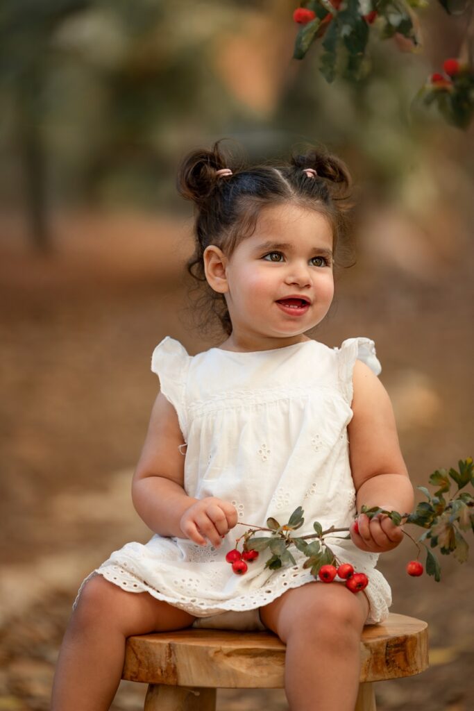 בת שנתיים יושבת על שרפרף בטבע עם ורדים ביד