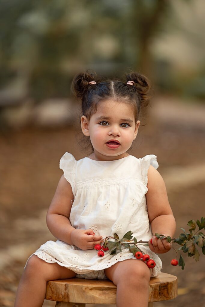 בת שנתיים יושבת על שרפרף בטבע עם ורדים ביד