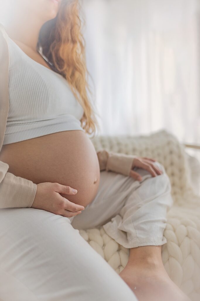צילומי היריון אישה בהריון יושבת ומחבקת את הבטן