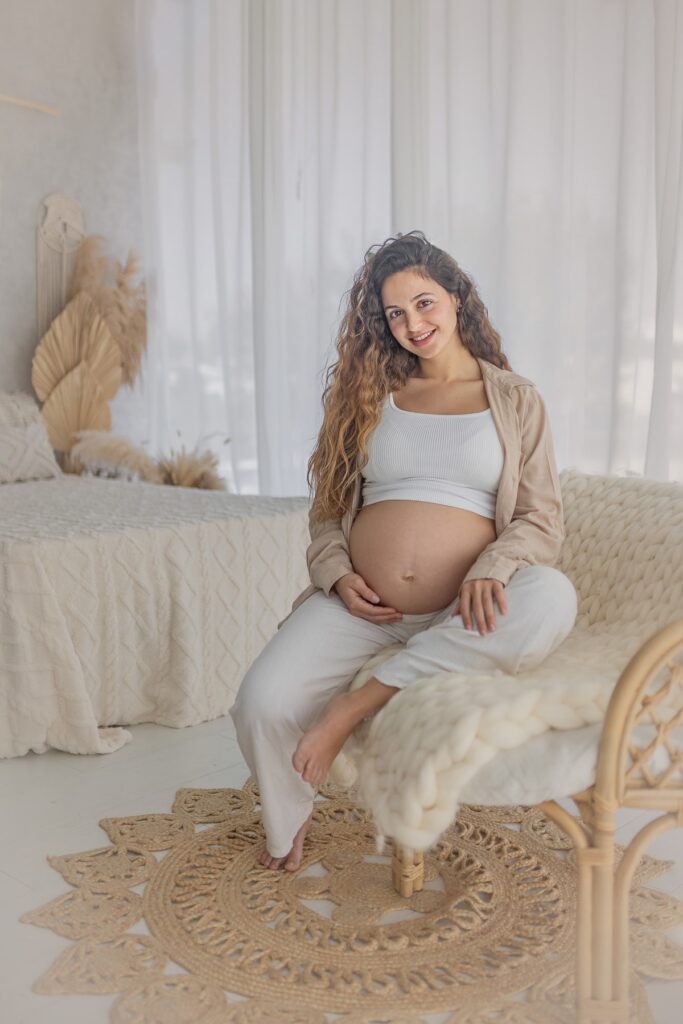 צילומי היריון אישה בהריון יושבת ומחבקת את הבטן
